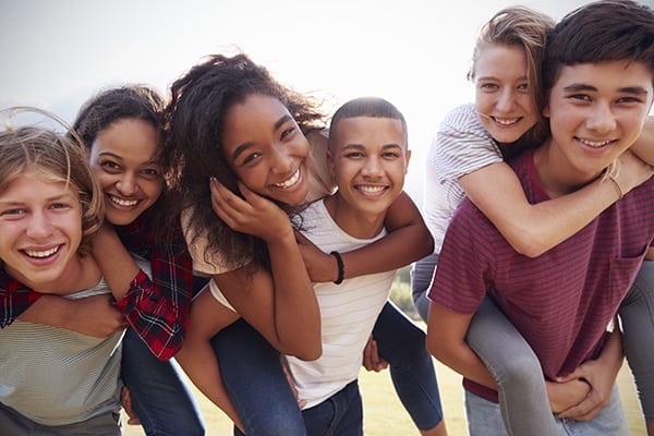 Teenage school friends having fun piggybacking outdoors